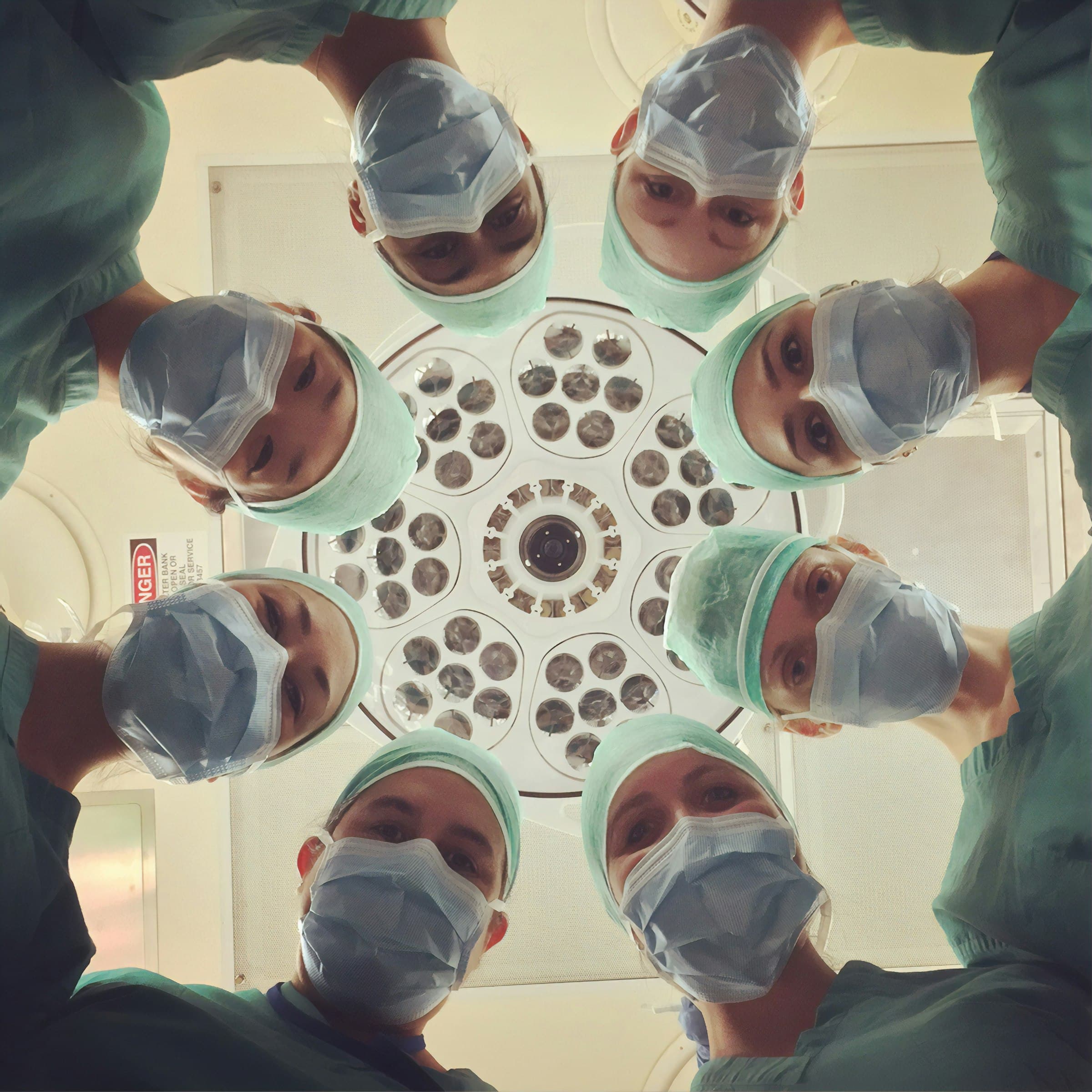 A surgical team in teal scrubs, seen from below the operating light